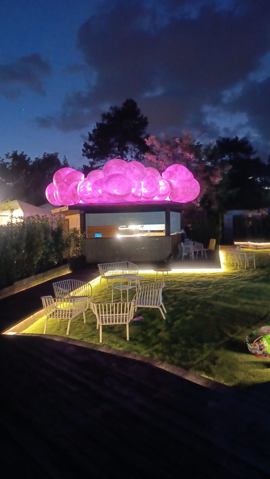 Spazio esterno al crepuscolo con installazione luminosa rosa e illuminazione calda a terra