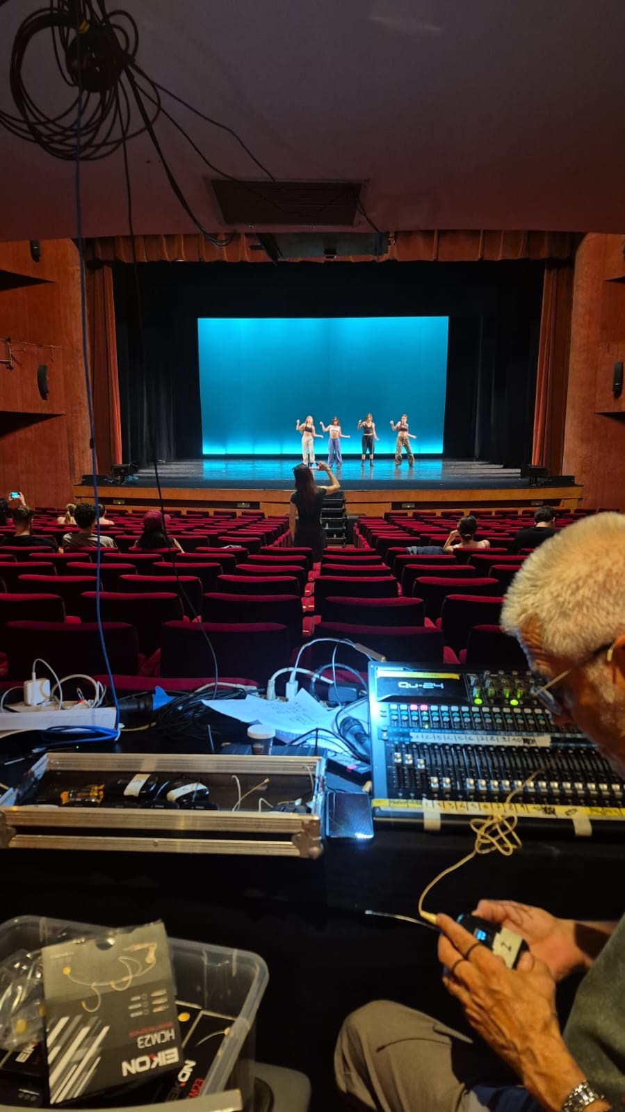 Regia audio in teatro con mixer e palco illuminato sullo sfondo